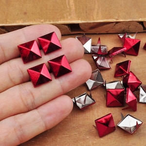 May include: A close-up of red pyramid-shaped studs with silver metal bases. The studs are arranged in a grid pattern on a wooden surface.