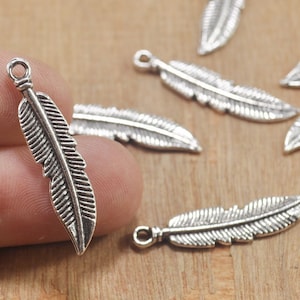 Op de afbeelding: Een set zilverkleurige verencharms. De charms zijn gedetailleerd met een getextureerd verenontwerp en hebben een lus aan de bovenkant om aan sieraden of andere knutselwerken te bevestigen.