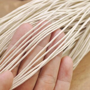 Può includere: Primo piano di un fascio di cordoncino di cotone cerato di colore crema naturale. Il cordoncino è sottile e liscio, ed è perfetto per l'artigianato e la creazione di gioielli.