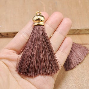 May include: A brown tassel with a gold metal top. The tassel is about 2 inches long and is made of soft, silky threads.