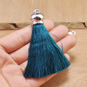 May include: Teal blue tassel with a silver metal top. The tassel is held in a hand.