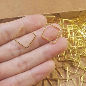 May include: Two gold-coloured metal square frames, one in each hand, with a pile of similar frames in the background.