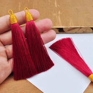 Könnte beinhalten: Drei rote Quastenbesätze mit goldenen Spitzen. Die Quasten bestehen aus weichen, feinen Fäden und sind etwa 5 cm lang.