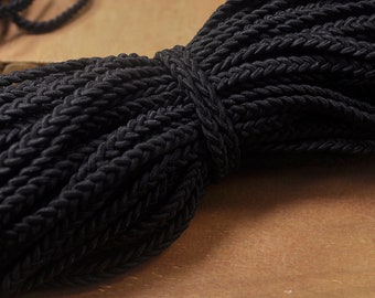 May include: A close-up of a black braided cord, showing the intricate woven pattern. The cord is thick and textured, with a soft, pliable feel.