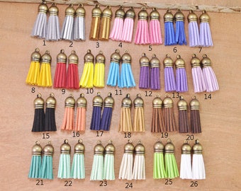 Puede incluir: Veintiséis pares de borlas de gamuza de colores vivos con tapas de metal dorado. Las borlas están dispuestas en filas sobre una superficie de madera.