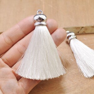 May include: Two white silk tassels with silver metal tops. The tassels are approximately 2 inches long.
