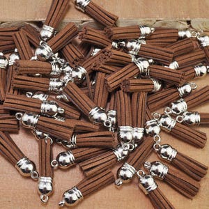 May include: A large group of brown suede tassels with silver metal caps. The tassels are arranged in a random pattern and are all the same size.