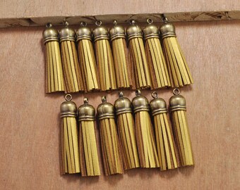 Puede incluir: Un conjunto de 18 borlas de cuero de color dorado con un patrón de rayas marrones y amarillas. Las borlas están dispuestas en dos filas sobre una superficie de madera.