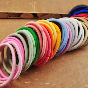 K&ouml;nnte beinhalten: Eine gro&szlig;e Auswahl an bunten Haargummis in verschiedenen Farbt&ouml;nen von Rosa, Gr&uuml;n, Blau, Gelb, Orange, Rot und Braun. Die Haargummis sind aus einem weichen, dehnbaren Material gefertigt und perfekt, um das Haar an Ort und Stelle zu halten.