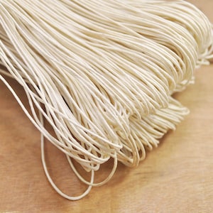 May include: A close-up of a bundle of natural cream-coloured twine. The twine is tightly wound and appears to be made of natural fibres.