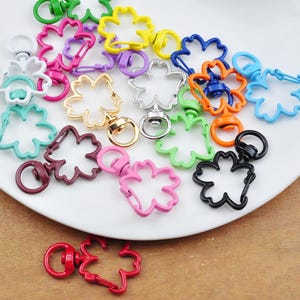 May include: Assortment of colourful metal keychains shaped like a flower with a swivel clasp. The keychains are in various colours, including red, orange, yellow, green, blue, purple, pink, and black.
