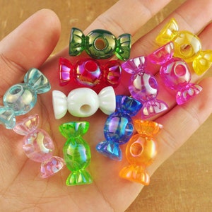 Peut inclure: Assortiment de perles en plastique colorées en forme de bonbons avec des finitions irisées. Les perles sont de différentes couleurs, notamment le vert, le rouge, le bleu, le jaune et le blanc.