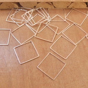 May include: A pile of silver-toned metal square hoops, scattered on a wooden surface.