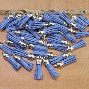 May include: A collection of blue suede tassels with silver metal caps. The tassels are scattered on a wooden surface.