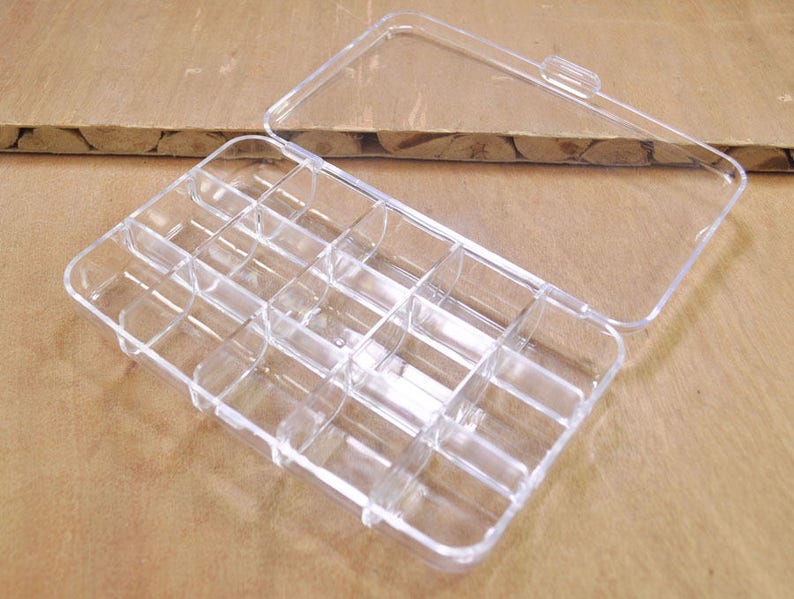 May include: A clear plastic storage box with a hinged lid and 12 compartments. The box is empty.