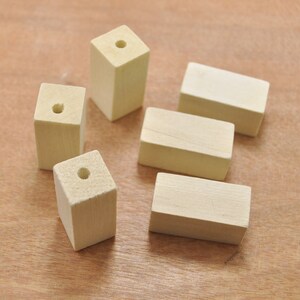 Puede incluir: Cinco bloques de madera sin terminar con un agujero perforado en el centro de cada bloque. Los bloques están dispuestos en un patrón escalonado sobre una superficie de madera marrón claro.