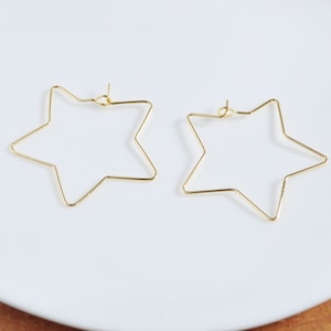 May include: A pair of gold star-shaped hoop earrings. The earrings are made of thin wire and have a simple, minimalist design.