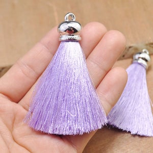 May include: Two lavender silk tassels with silver metal caps. The tassels are about 2 inches long and are held in a hand.