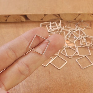 Puede incluir: Primer plano de un anillo de salto cuadrado plateado, con una pila de anillos de salto similares en el fondo.