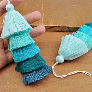 May include: Two ombre tassel charms with a gradient of blue, teal, and green colors. The tassels are made of soft yarn and have a delicate, layered look.