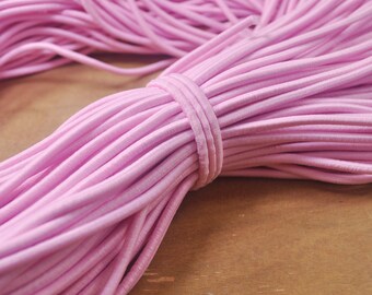 Peut inclure: Un gros paquet de cordon élastique rose. Le cordon est enroulé serré et a une finition lisse et brillante.
