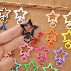 May include: A selection of star-shaped swivel clasps in diverse colours: silver, white, blue, black, red, peach, orange, yellow, pink, purple, and green. Each clasp features a ring for attaching to keychains or other items.