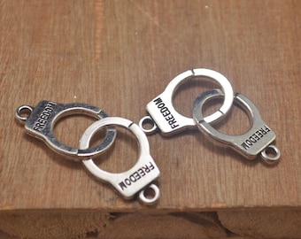 Pode incluir: Três pingentes de metal prateado em forma de algemas com a palavra "FREEDOM" gravada em cada um. Os pingentes estão ligados entre si.
