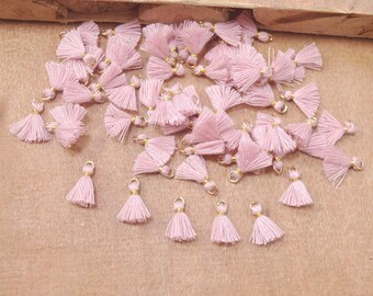 May include: A large group of pink tassel charms with gold jump rings. The tassels are made of soft, fluffy yarn and are perfect for adding a touch of whimsy to jewelry, bags, or other crafts.