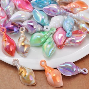 May include: A collection of small, iridescent seashell-shaped charms in various pastel colors including pink, blue, green, purple, and orange. Each charm features a smooth, glossy finish and a small circular loop at the top for attachment.