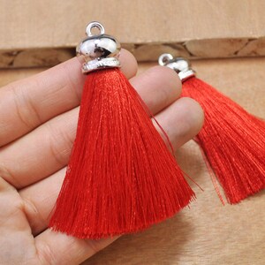 May include: Two red tassel ornaments with silver metal tops. The tassels are made of soft, silky threads and are approximately 2 inches long.