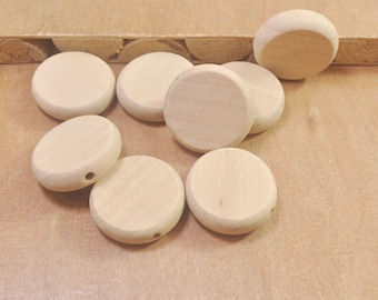 May include: A group of eight unfinished wooden circles with a hole in the center. The circles are arranged in a random pattern on a light brown wooden surface.