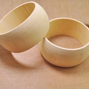 May include: Two unfinished wooden bangles, one stacked on top of the other. The bangles are round and have a smooth surface.