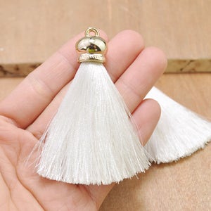 May include: Two white tassel ornaments with gold metal tops. The tassels are made of soft, silky threads and are approximately 2 inches long.