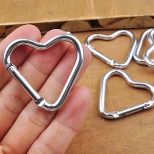 May include: A set of six silver heart-shaped keychains. The keychains are made of metal and have a smooth finish.