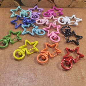 Puede incluir: Un conjunto de llaveros de metal con forma de estrella en varios colores con cierres giratorios. Los llaveros están hechos de metal y vienen en una variedad de colores, incluyendo rojo, naranja, amarillo, verde, azul, morado, rosa y negro.