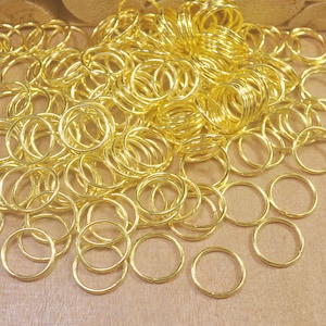 May include: A large pile of gold-colored metal jump rings. The rings are all the same size and are arranged in a random pattern.