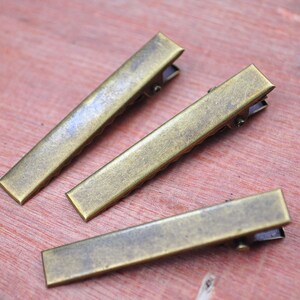 May include: Three antique gold metal hair clips. The clips are rectangular and have a textured surface.