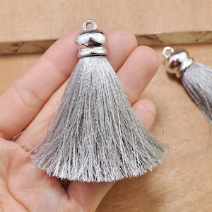 May include: Two silver tassel pendants with a silver metal top. The tassels are made of a soft, gray material.