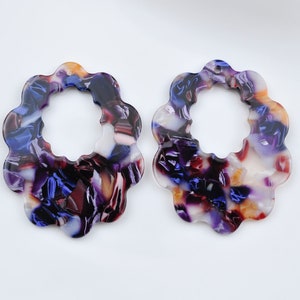 Può includere: Due orecchini in resina a forma di fiore con un motivo a spirale viola, bianco e arancione e un foro nella parte superiore.