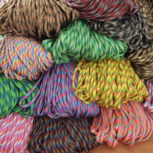 May include: A collection of colorful paracord bundles in various shades, including green, yellow, blue, pink, and brown. The cords are tightly wound, showcasing a variety of patterns and color combinations. The image is a close-up, highlighting the texture and detail of the cords.