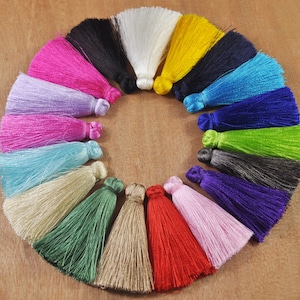 May include: A collection of 16 colorful tassels arranged in a circle. The tassels are made of soft, silky yarn and come in a variety of colors, including pink, purple, blue, green, yellow, red, and white.