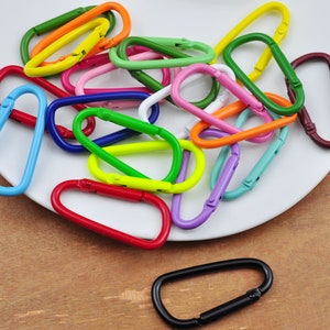 May include: A collection of colorful metal key rings in various shapes and sizes. The key rings are arranged on a white plate.