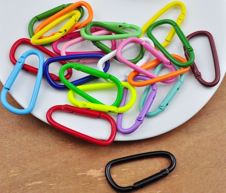 May include: A collection of colorful metal key rings in various shapes and sizes. The key rings are arranged on a white plate.