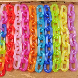 Può includere: Un set di dieci catene di plastica colorate, ogni catena è di un colore diverso, tra cui rosso, rosa, arancione, giallo, verde, blu, viola e bianco. Le catene sono tutte della stessa lunghezza e sono disposte in fila.