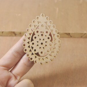 Può includere: Un ritaglio di legno a forma di ovale con un design decorativo. Il design presenta un cerchio centrale circondato da cerchi e triangoli più piccoli.