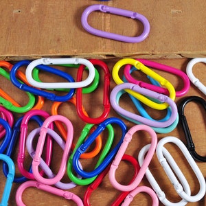 May include: A collection of colorful metal key rings in various shapes and sizes. The key rings are arranged in a random pattern on a wooden surface.