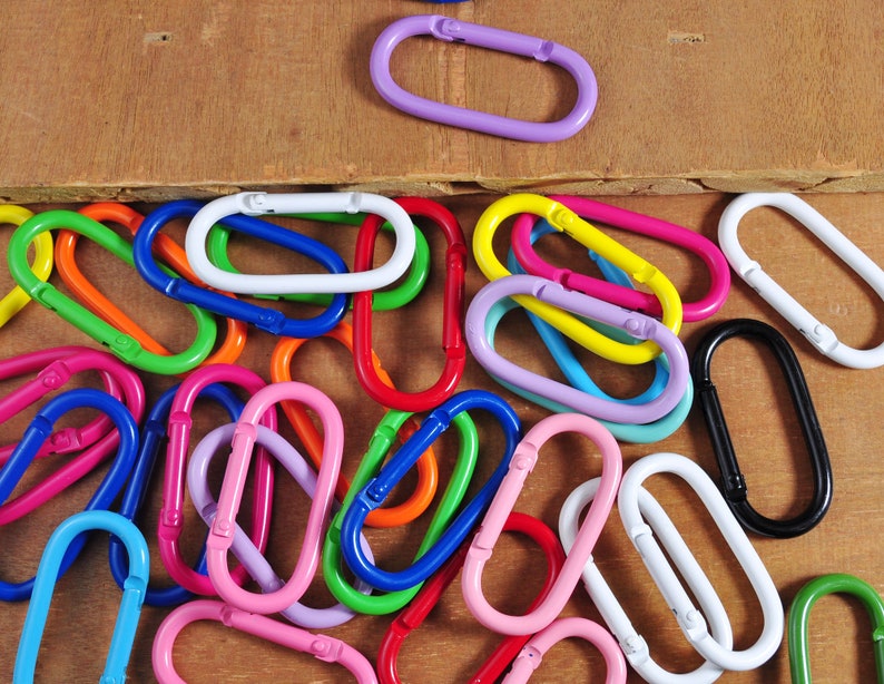 May include: A collection of colorful metal key rings in various shapes and sizes. The key rings are arranged in a random pattern on a wooden surface.