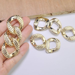 Puede incluir: Eslabones de cadena de metal dorado con superficie texturizada. Los eslabones son de varias formas y tamaños, incluyendo ovalados y cuadrados.