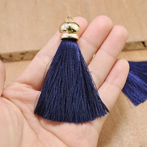 May include: A dark blue tassel with a gold metal top. The tassel is made of soft, silky threads and is approximately 2 inches long.