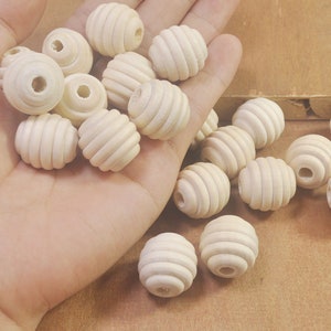 Puede incluir: Una colección de cuentas de madera con textura acanalada. Las cuentas son de color crema claro y están dispuestas en una mano.